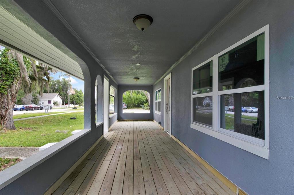 A covered porch features a wooden deck, gray walls, and arched openings looking toward a street — 500 N 13TH STREET, LEESBURG, FL