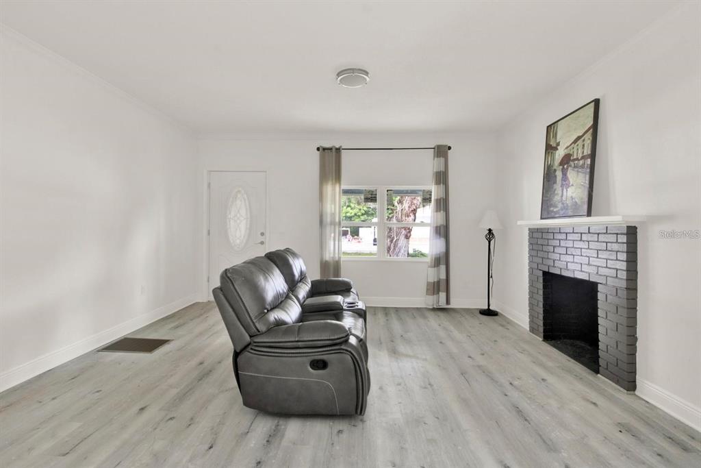 A living room features light wood-look flooring, a gray reclining sofa, and a brick fireplace — 500 N 13TH STREET, LEESBURG, FL