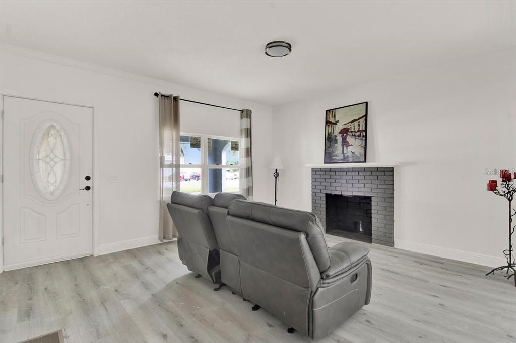 A living room features light wood-look flooring, a grey brick fireplace, and a grey sofa — 500 N 13TH STREET, LEESBURG, FL