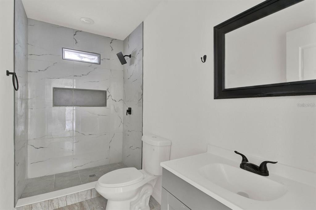 A bathroom features a walk-in shower with marble-look tile, a toilet, and a vanity — 500 N 13TH STREET, LEESBURG, FL