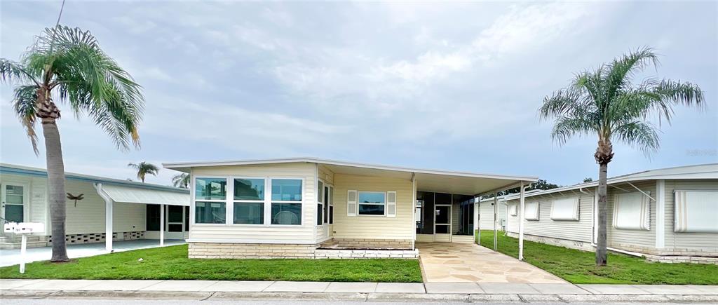 A light yellow manufactured home features a front sunroom, a carport, and two palm trees — 1100 BELCHER ROAD S UNIT 787, LARGO, FL