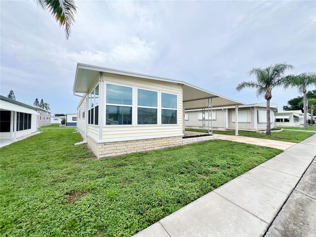 A light-colored mobile home features a large sunroom, a carport, and a stone-patterned base — 1100 BELCHER ROAD S UNIT 787, LARGO, FL