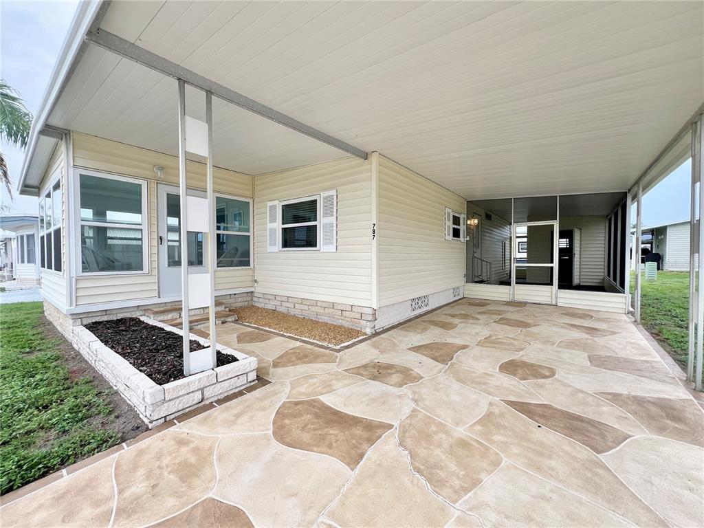 A mobile home exterior features a patterned concrete driveway, a covered carport, and a small planter — 1100 BELCHER ROAD S UNIT 787, LARGO, FL