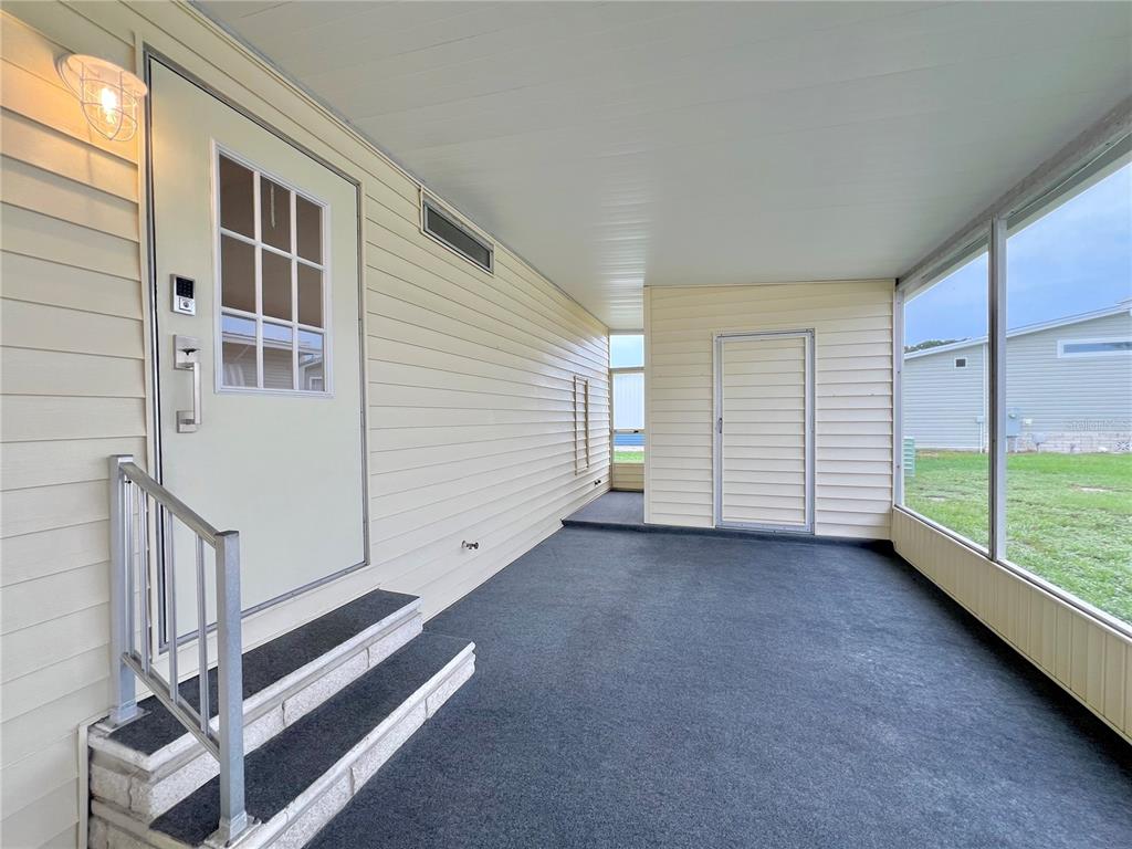 A covered, screened-in porch features light-colored siding, a carpeted floor, and a set of stairs — 1100 BELCHER ROAD S UNIT 787, LARGO, FL
