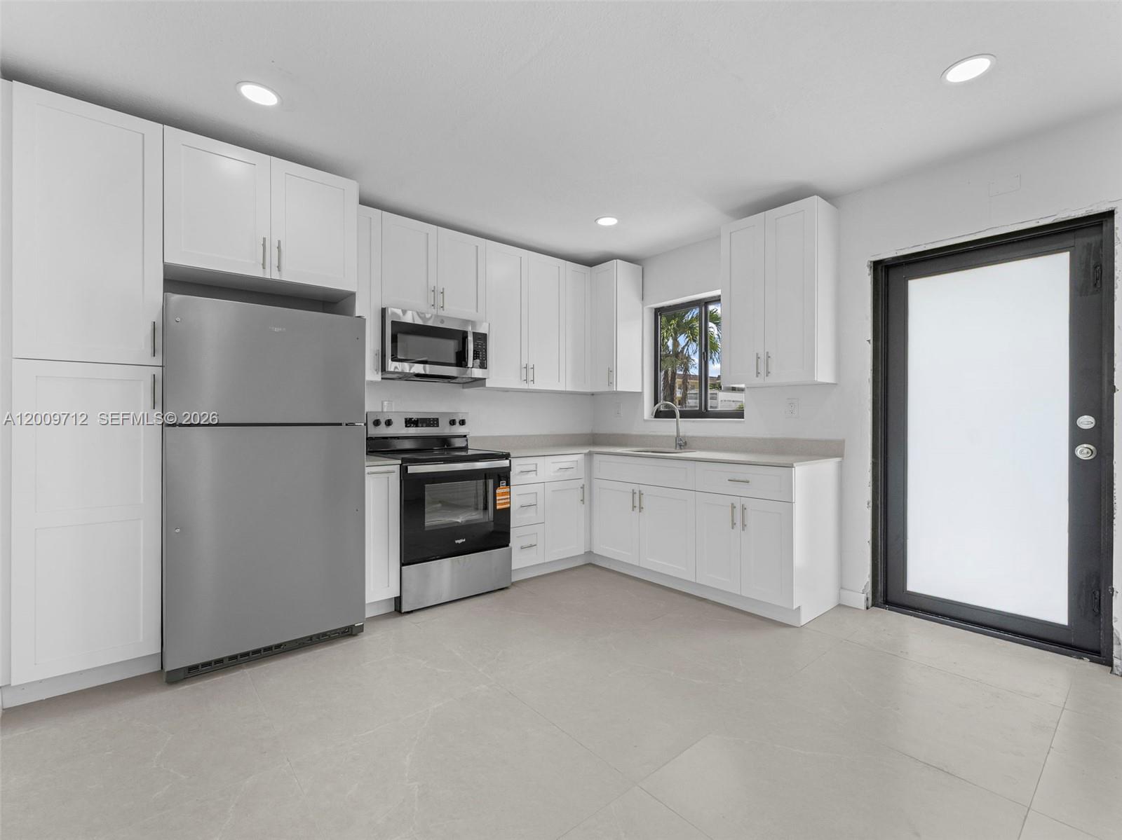 A kitchen features white cabinetry, stainless steel appliances, light countertops, and a glass-paneled door — 1368 W 29th St # 2, Hialeah FL 33012, HIALEAH, FL