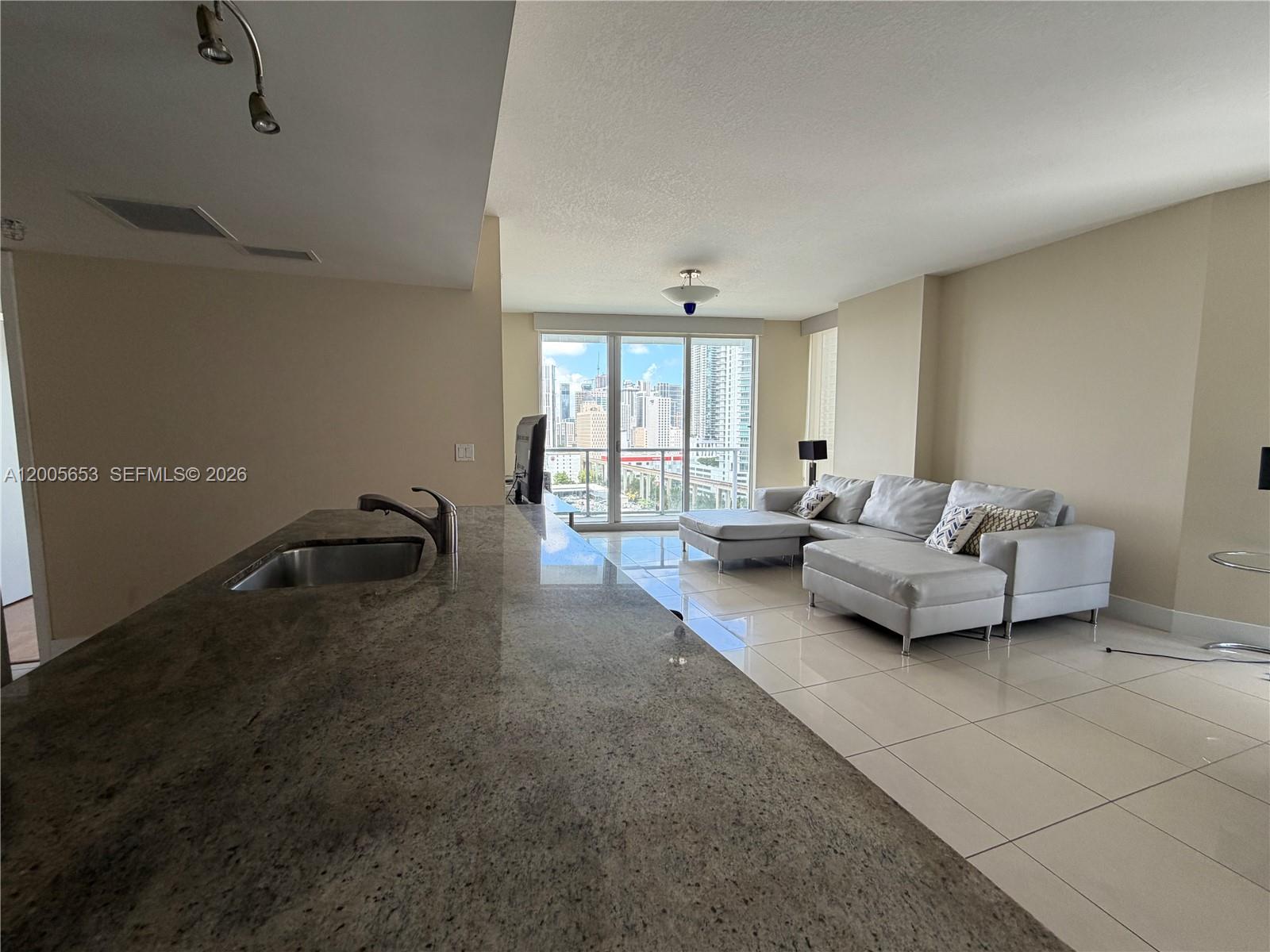 A kitchen island with a granite countertop overlooks a living area with a city view — 185 SW 7th St # 1511, Miami FL 33130, MIAMI, FL