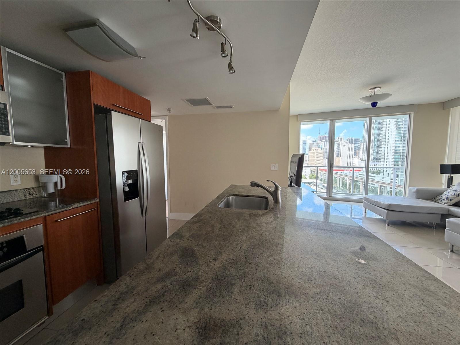 A kitchen with granite countertops and stainless steel appliances overlooks a living area with city views — 185 SW 7th St # 1511, Miami FL 33130, MIAMI, FL