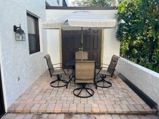 A patio features a table with four chairs under a striped umbrella against a white wall — 5056 MARSH FIELD ROAD UNIT 7, SARASOTA, FL