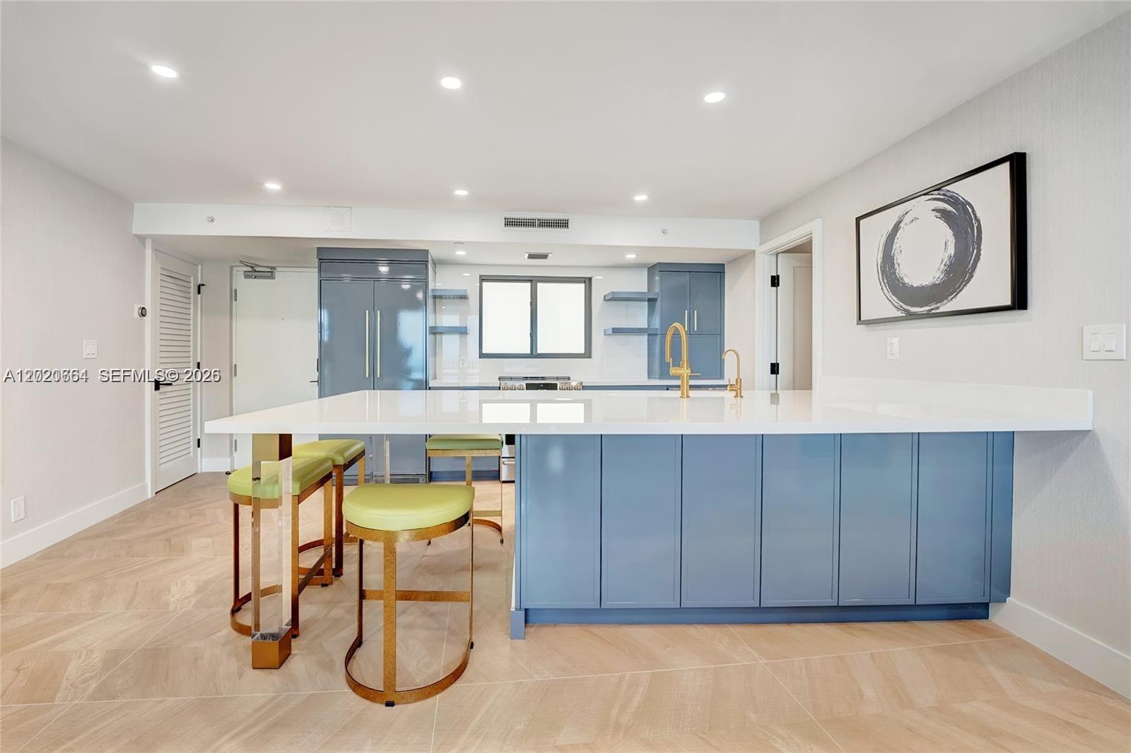 A modern kitchen features blue cabinets, a white island, and lime green bar stools — 300 Ocean Trail Way # 702, Jupiter FL 33477, JUPITER, FL