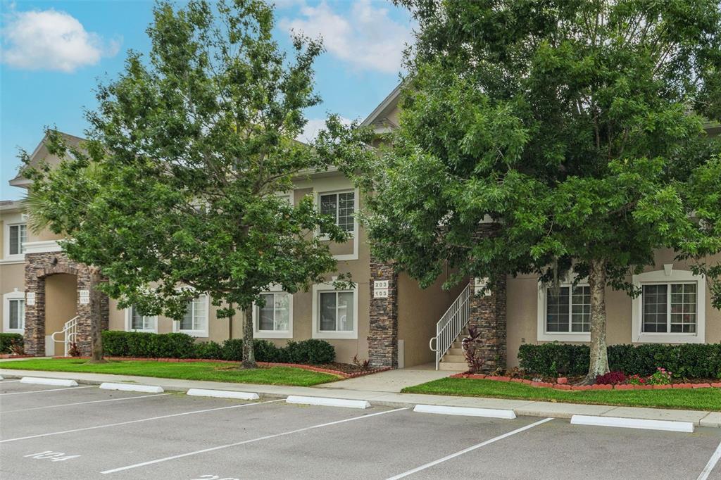 A multi-story apartment building with tan stucco, stone accents, and a parking lot in front — 1231 GODAVARI WAY UNIT 204, WESLEY CHAPEL, FL