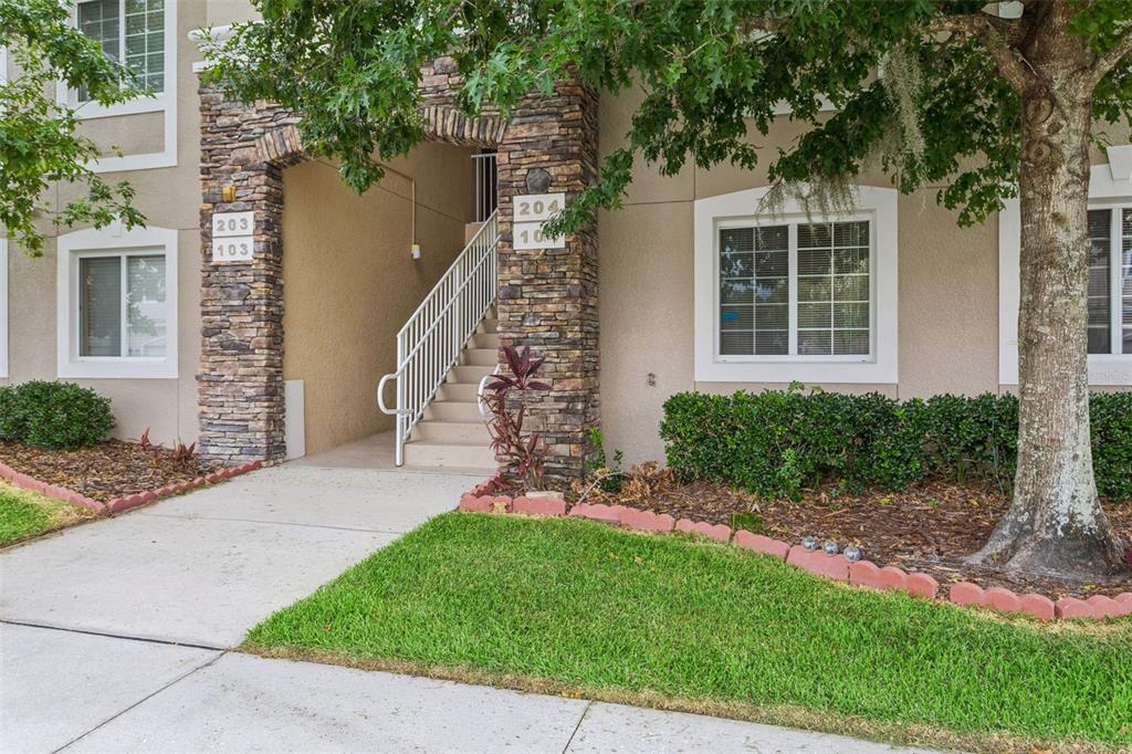 An exterior view of a multi-story apartment building entrance with stone accents and stairs — 1231 GODAVARI WAY UNIT 204, WESLEY CHAPEL, FL
