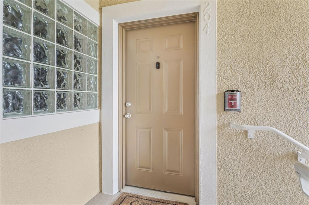 A beige entry door with a glass block wall and a fire alarm pull station — 1231 GODAVARI WAY UNIT 204, WESLEY CHAPEL, FL