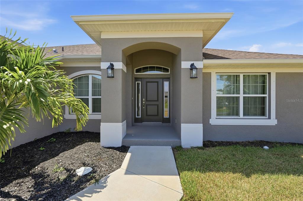 The exterior of a house features a gray stucco facade, a covered entryway, and windows — 119 LONG MEADOW LANE, ROTONDA WEST, FL