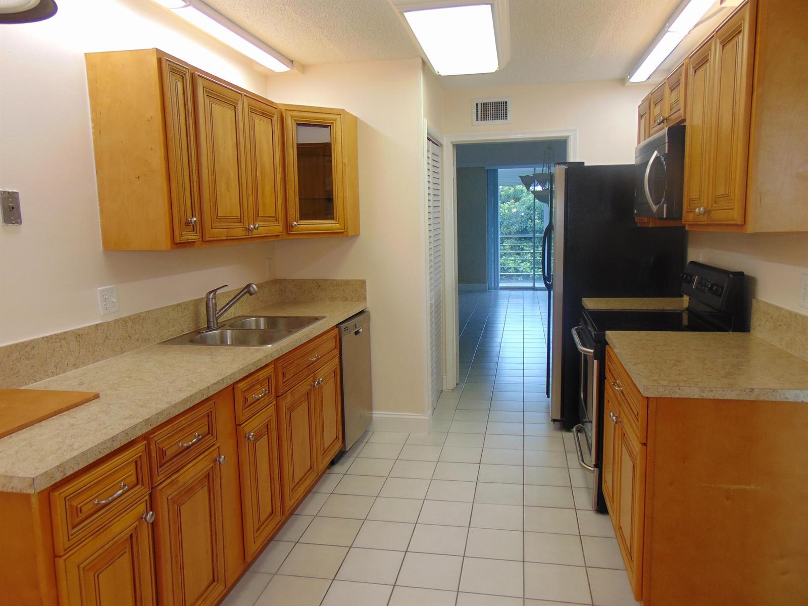 A galley kitchen features light wood cabinets, beige countertops, black appliances, and white tile flooring — 3286 Arcara Way # 413, FL 33467, FL