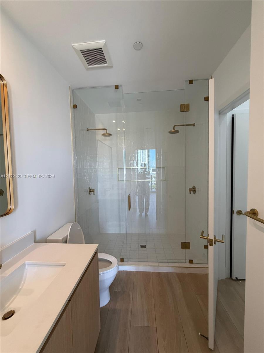 A bathroom features a glass-enclosed shower, a vanity with a sink, and wood-look flooring — 90 NE 32nd ST # 1110, Miami FL 33145, MIAMI, FL