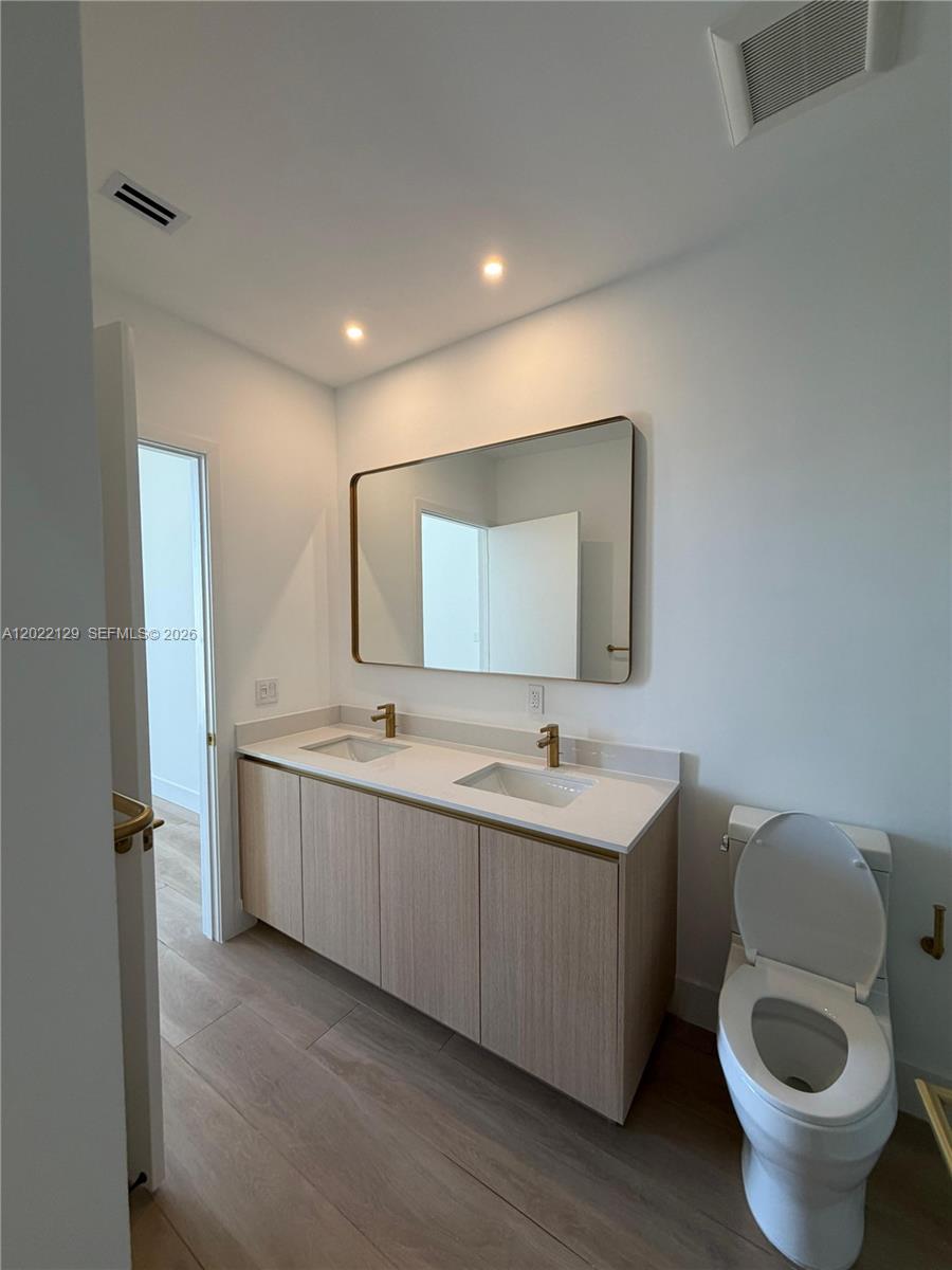 A modern bathroom features a double-sink vanity with light wood cabinets and gold fixtures — 90 NE 32nd ST # 1110, Miami FL 33145, MIAMI, FL