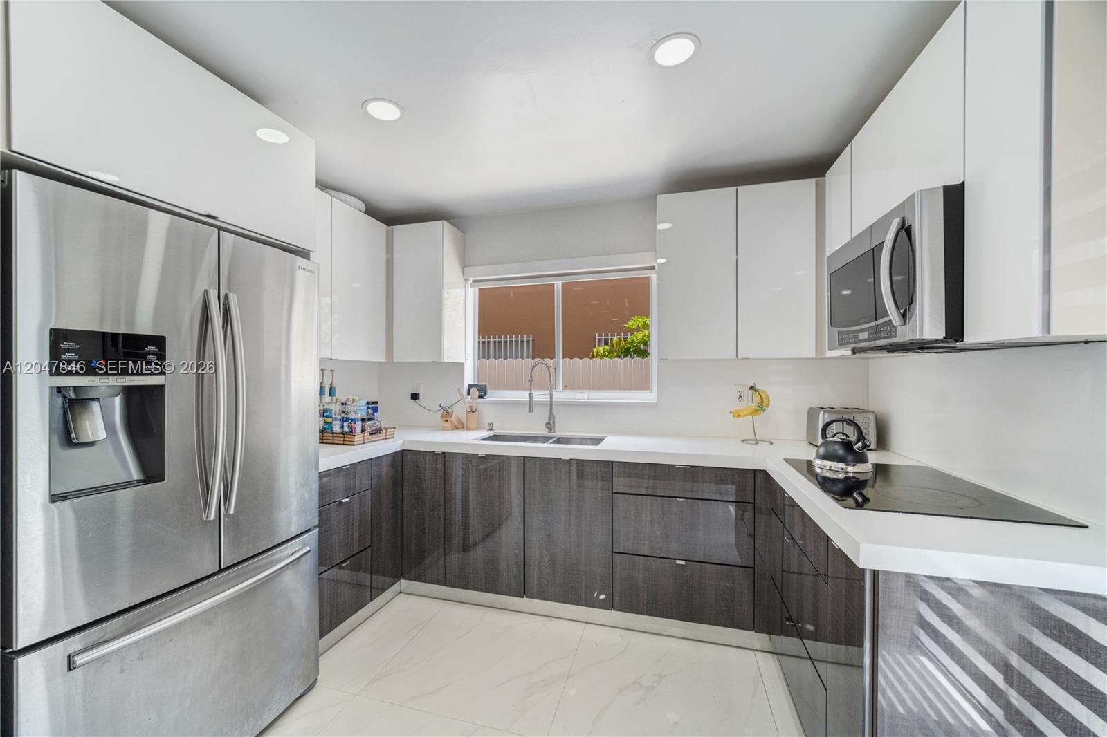A modern kitchen features white upper cabinets, dark gray lower cabinets, and stainless steel appliances — 8668 NW 2nd Ter, Miami FL 33126, MIAMI, FL