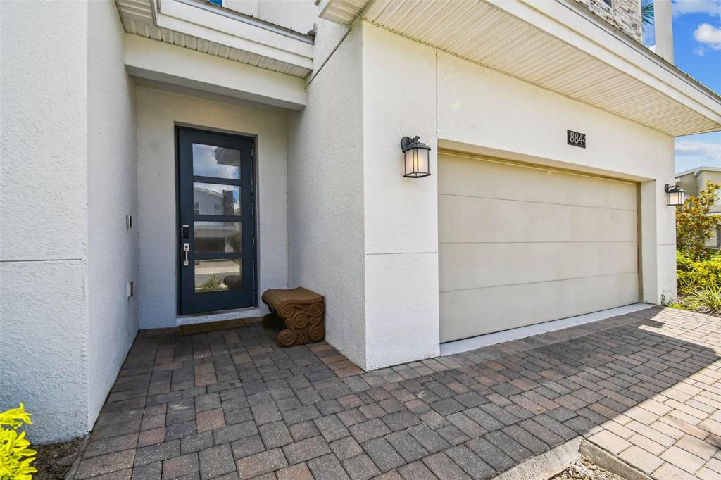 A paved walkway leads to a dark glass-paneled front door and a beige garage door — 8844 CRUDEN BAY COURT, DAVENPORT, FL