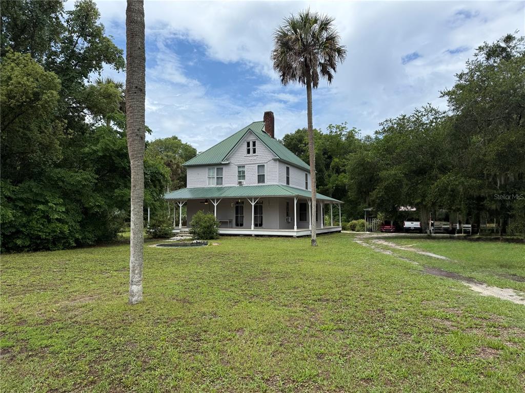 A two-story house with a green metal roof and a wrap-around porch sits outdoors — 110 N VOLUSIA AVENUE, PIERSON, FL