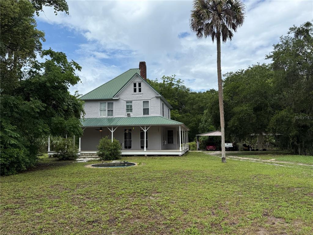 A two-story house with a green metal roof and a wrap-around porch sits on grass — 110 N VOLUSIA AVENUE, PIERSON, FL
