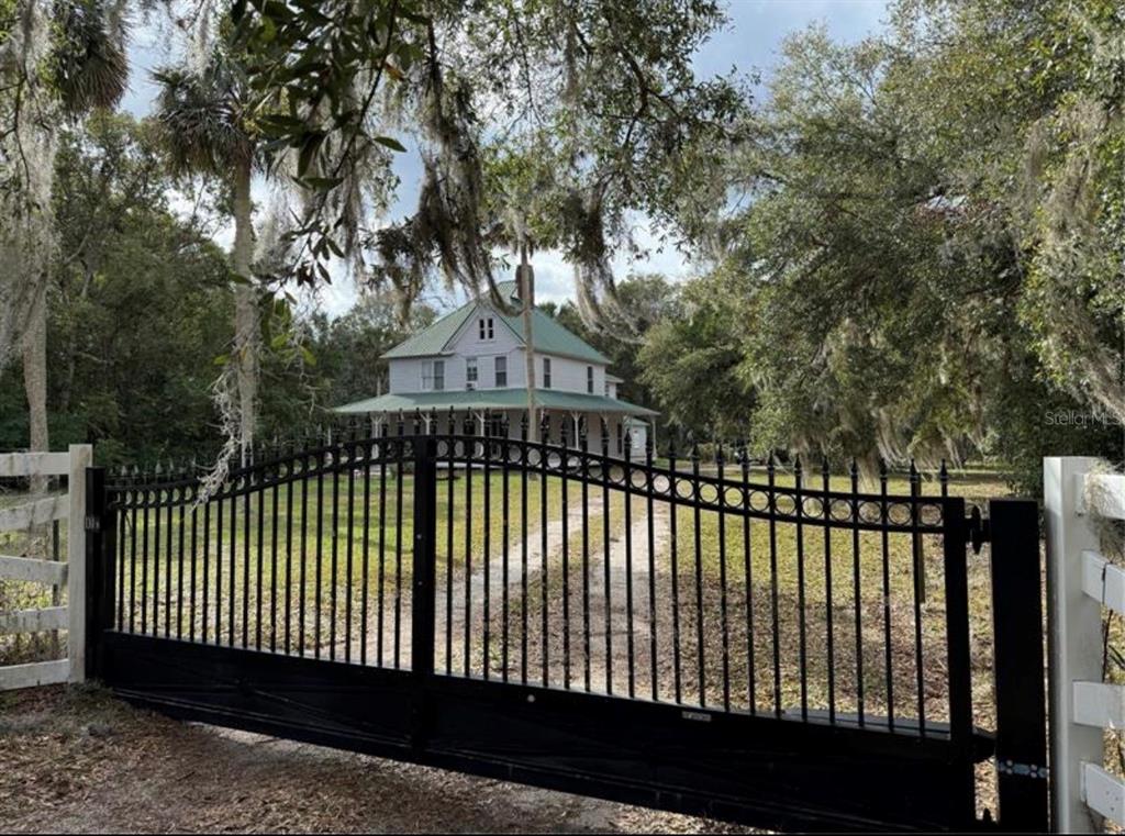 A two-story white house with a green roof sits behind a black metal gate — 110 N VOLUSIA AVENUE, PIERSON, FL