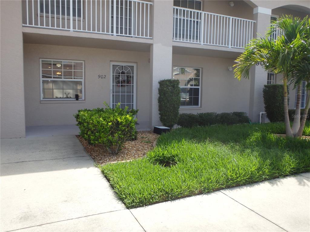 A tan two-story building exterior features a ground-level entrance, windows, and a small front lawn — 11644 SW EGRET CIRCLE UNIT 902, LAKE SUZY, FL
