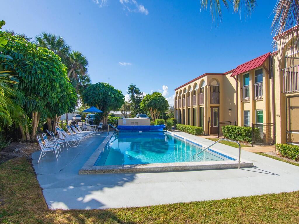An outdoor swimming pool sits beside a multi-story apartment building with a red roof — 4150 Highway A1A # 101, Vero Beach FL 32963, VERO BEACH, FL