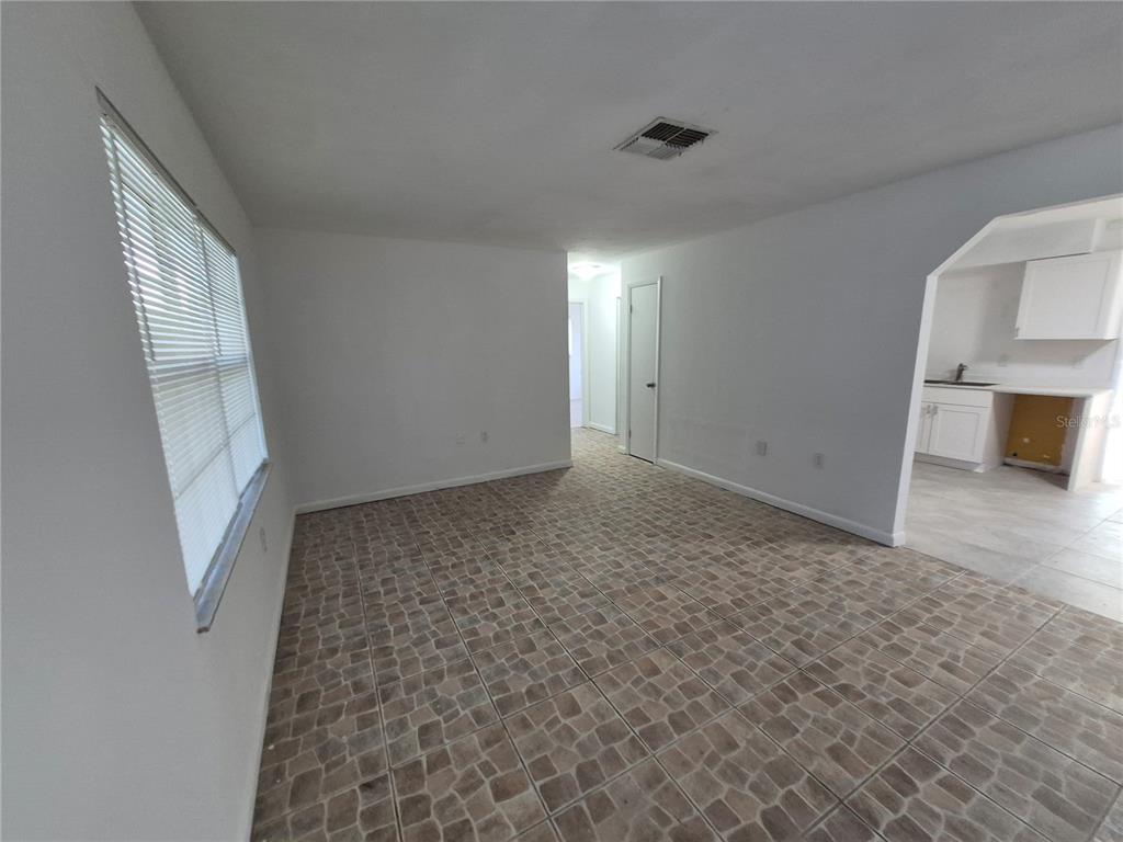 An empty room with tiled flooring, white walls, and a view into a kitchen — 9 MICHIGAN STREET, BEVERLY HILLS, FL