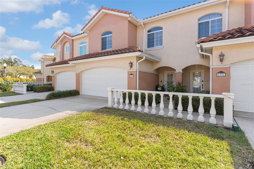 A two-story townhouse exterior features a white garage door, a balustrade fence, and stucco walls — 6339 VISTA VERDE DRIVE E, GULFPORT, FL