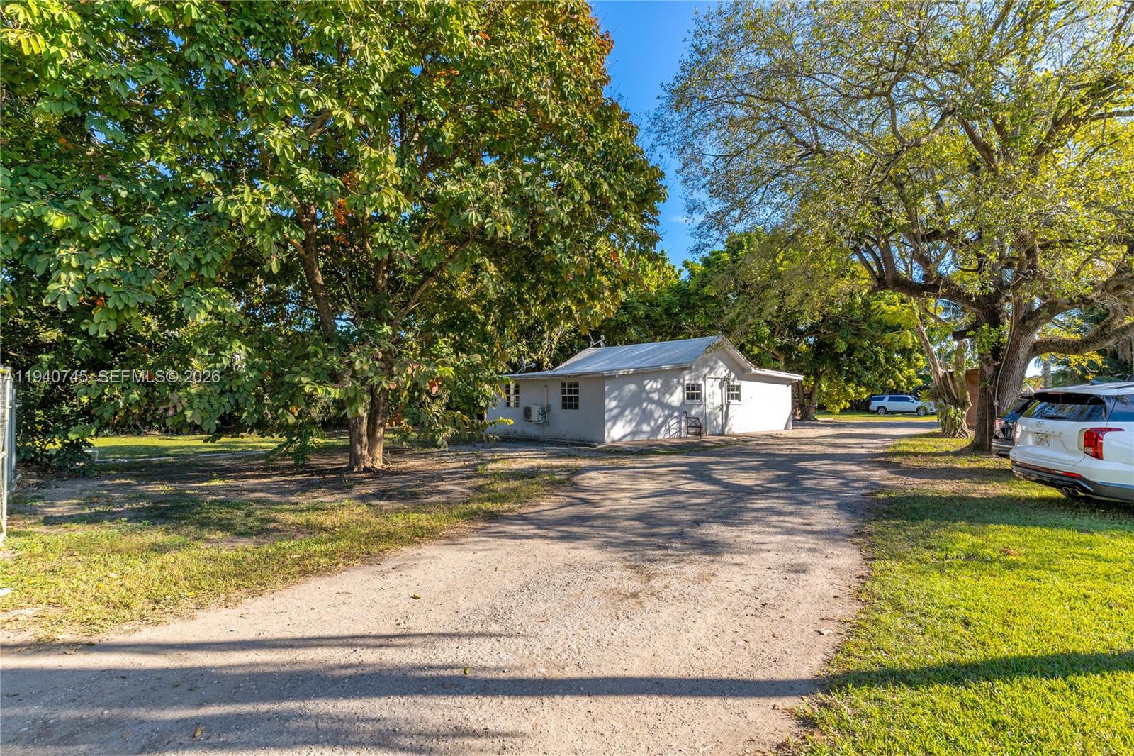 A white detached building sits on a gravel driveway surrounded by large trees — 19750 SW 136th St, Miami FL 33196, MIAMI, FL