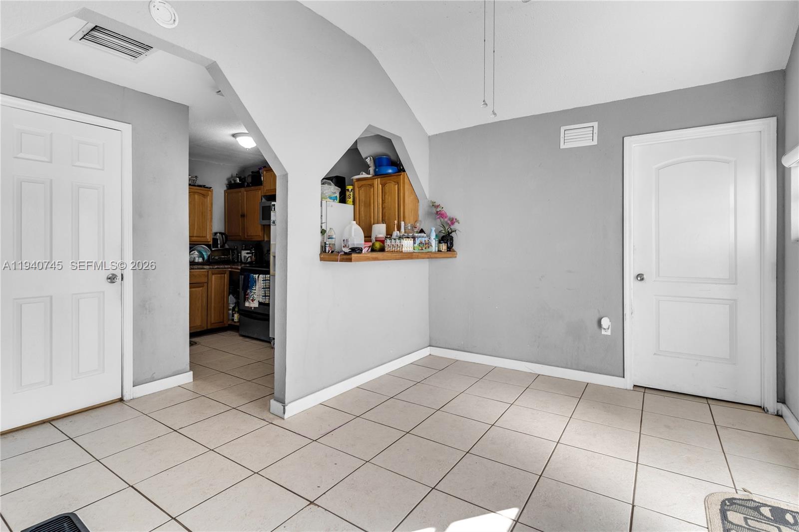 A room with light-colored tile flooring, gray walls, and a pass-through opening to a kitchen — 19750 SW 136th St, Miami FL 33196, MIAMI, FL