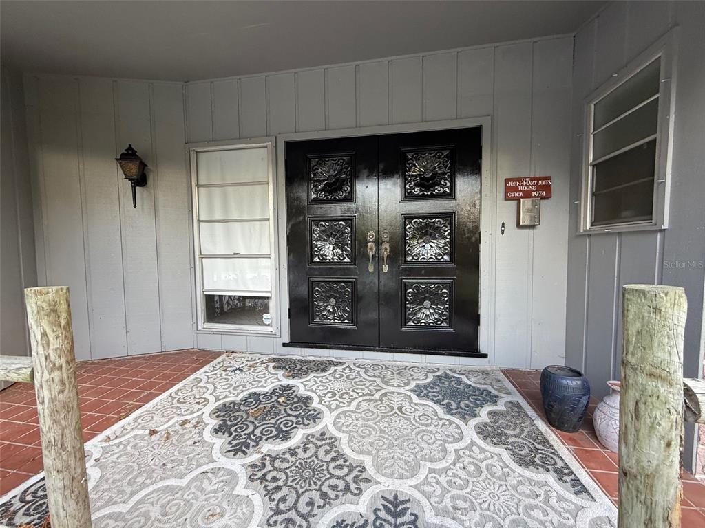 A covered porch features a patterned rug, terracotta tile flooring, and black double entry doors — 15300 LAKE IOLA ROAD, DADE CITY, FL