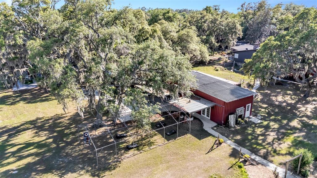An aerial view of a red metal-sided building with a screened-in patio and large trees — 15300 LAKE IOLA ROAD, DADE CITY, FL