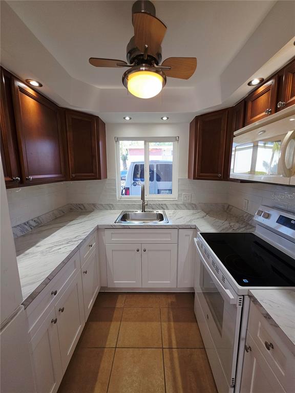 A galley kitchen features white cabinets, marble-look countertops, a stainless steel sink, and a ceiling fan — 4580 OVERLOOK DRIVE NE UNIT 190, ST PETERSBURG, FL