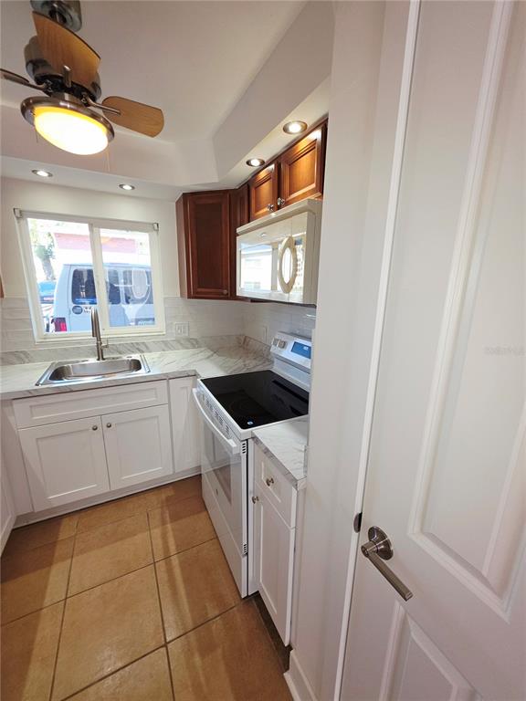 A kitchen features white cabinets, a stainless steel sink, a stove, and brown tile flooring — 4580 OVERLOOK DRIVE NE UNIT 190, ST PETERSBURG, FL