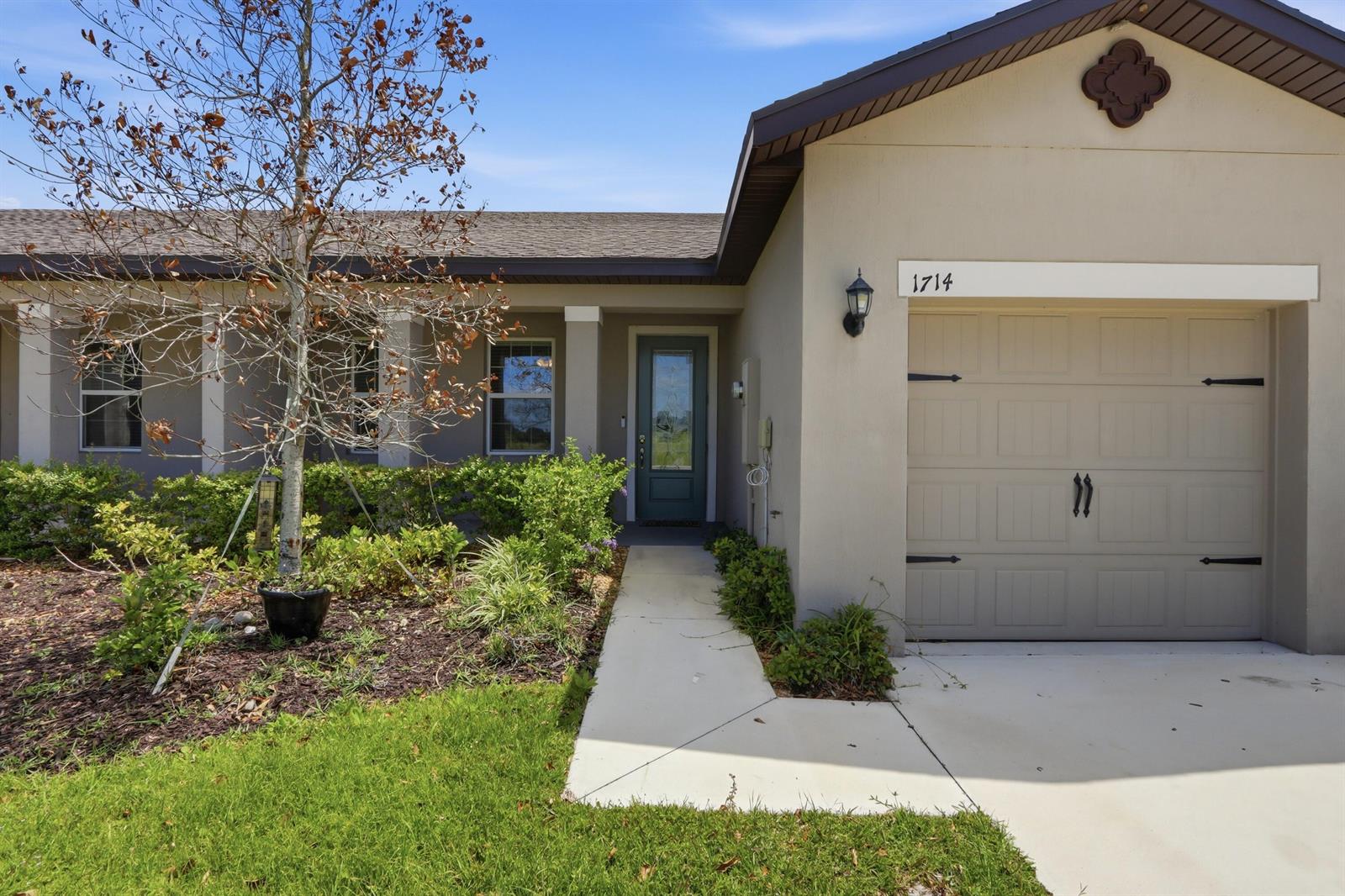 The exterior of a single-story house features a garage, a front walkway, and landscaping — 1714 Celebration Drive, Fort Pierce FL 34947, FORT PIERCE, FL
