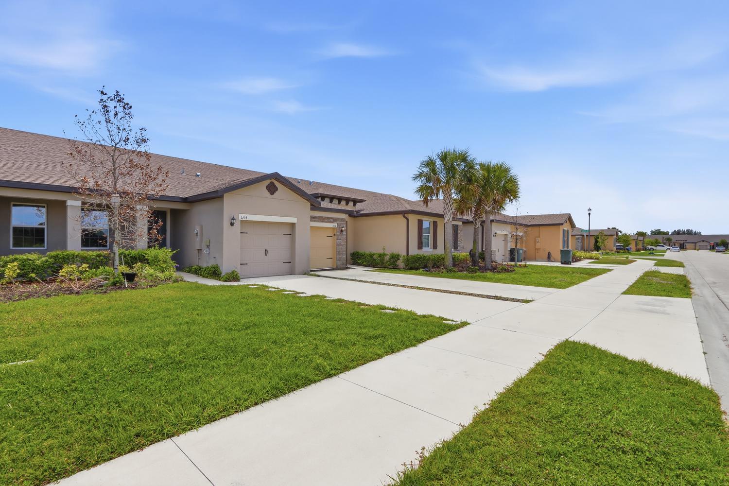 An exterior view of a row of single-story townhomes with garages and concrete driveways — 1714 Celebration Drive, Fort Pierce FL 34947, FORT PIERCE, FL