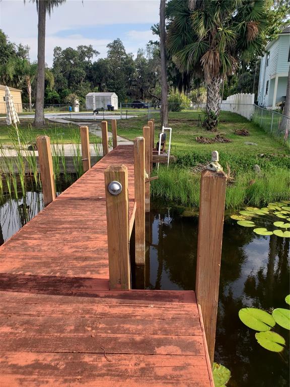A wooden dock extends over a pond with lily pads toward a grassy backyard — 17101 ARROWHEAD BOULEVARD, WINTER GARDEN, FL