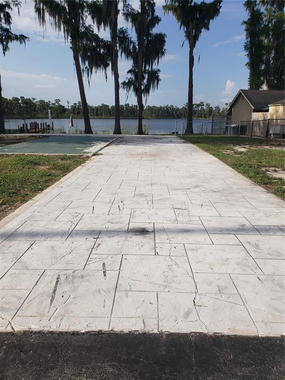 A stamped concrete driveway leads toward a lake with trees and a house in the background — 17101 ARROWHEAD BOULEVARD, WINTER GARDEN, FL