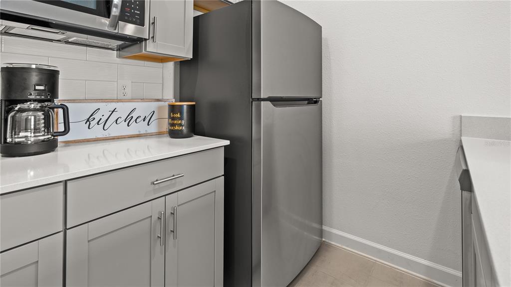 A kitchen features gray cabinets, white countertops, a stainless steel refrigerator, and a coffee maker — 3994 EASTMINSTER ROAD, DAVENPORT, FL
