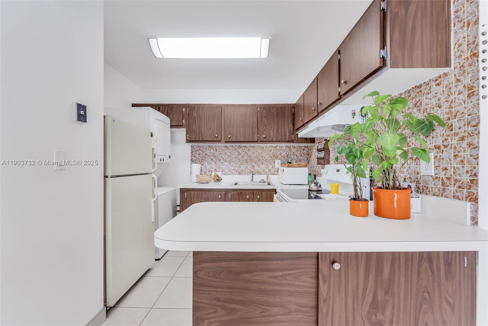 A kitchen features wood-tone cabinets, white countertops, a tiled backsplash, and a white refrigerator — 3661 SW 9th Ter # 402, Miami FL 33135, MIAMI, FL