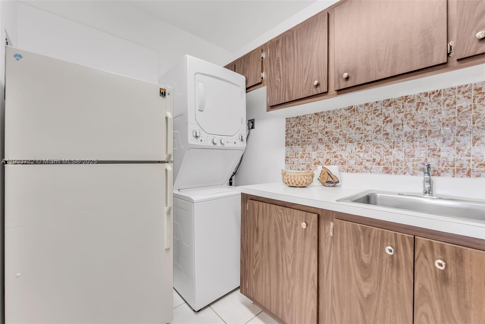 A laundry room features a stacked washer-dryer, a white refrigerator, and wood-grain cabinets — 3661 SW 9th Ter # 402, Miami FL 33135, MIAMI, FL