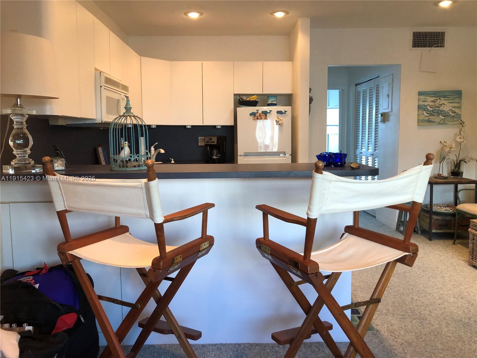 A kitchen features white cabinets, a dark countertop, and two wooden director's chairs — 1801 S Surf Rd # 4, Hollywood FL 33019, HOLLYWOOD, FL