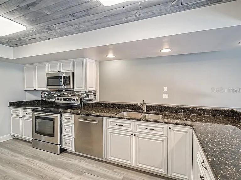 A kitchen features white cabinetry, stainless steel appliances, dark countertops, and a wood-plank ceiling — 4314 ELLENVILLE PLACE, VALRICO, FL