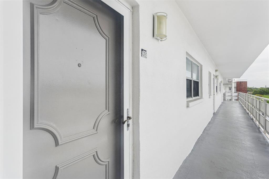 A gray door with a number 402 sign sits along an outdoor apartment building walkway — 5501 80TH STREET N UNIT 402, ST PETERSBURG, FL
