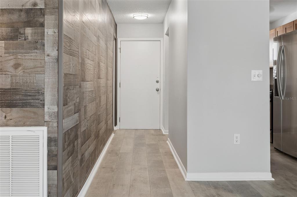 A hallway features a wood-paneled accent wall, light-colored flooring, and a white entry door — 5501 80TH STREET N UNIT 402, ST PETERSBURG, FL