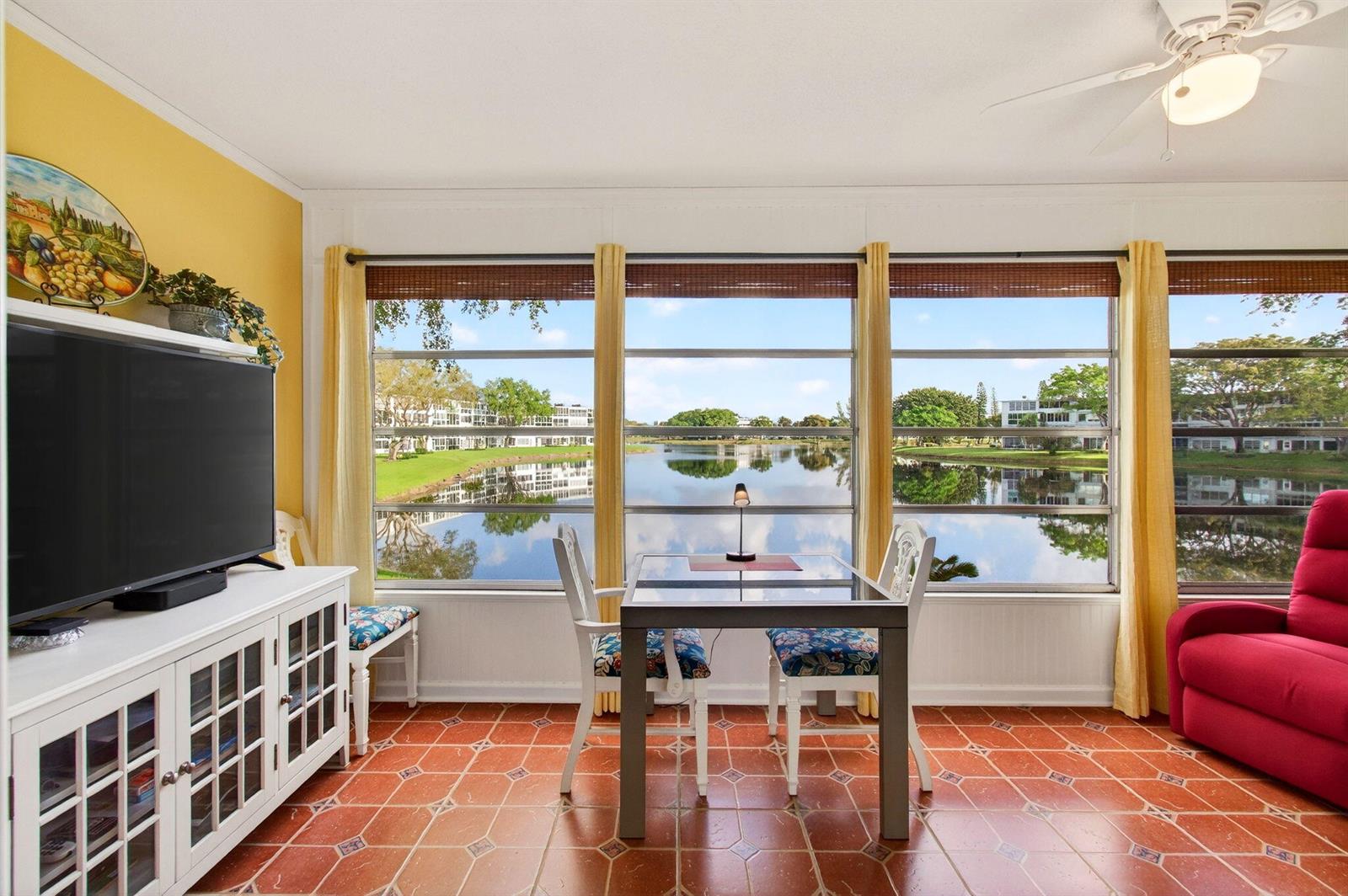 A sunroom with terracotta tile floors, a dining set, and large windows overlooking a lake — 2073 Cambridge D, Deerfield Beach FL 33442, DEERFIELD BEACH, FL