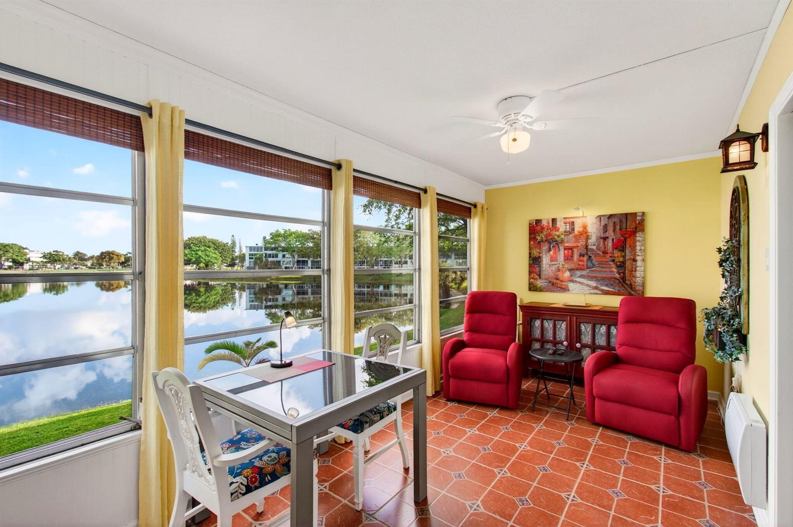 A sunroom features red recliners, a dining table, tile floors, and large windows overlooking water — 2073 Cambridge D, Deerfield Beach FL 33442, DEERFIELD BEACH, FL