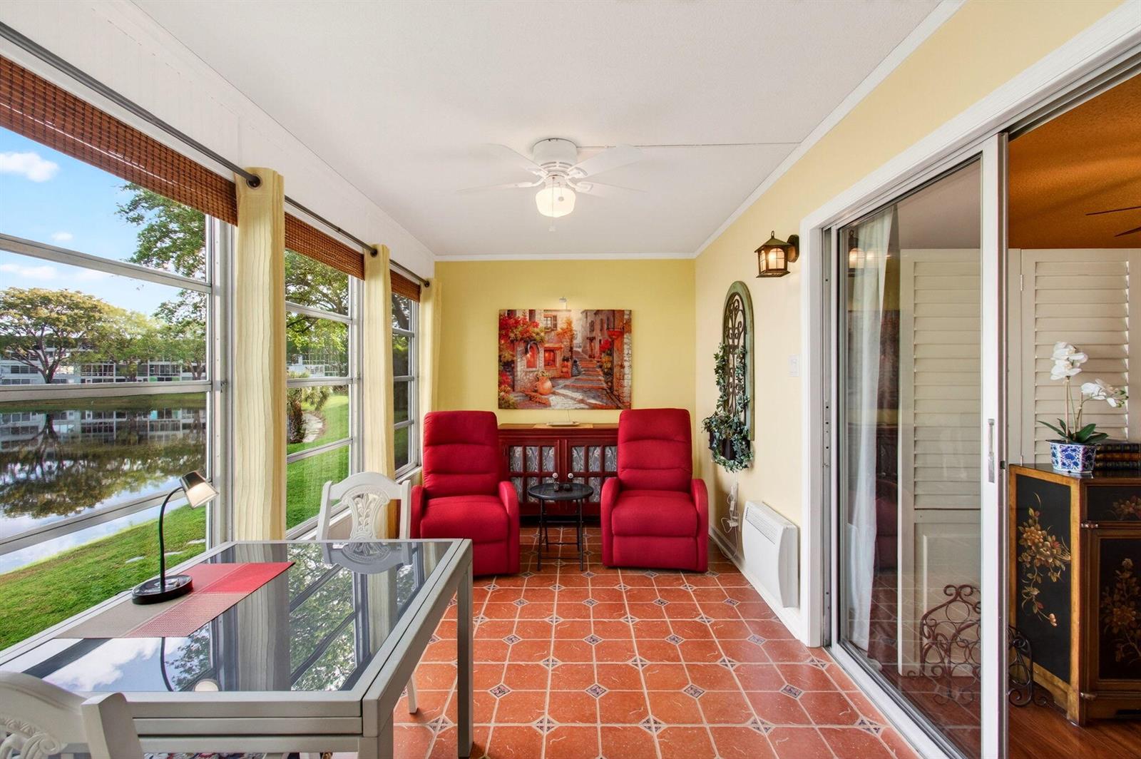 A sunroom with red recliners, a glass table, and tile floors overlooks a pond — 2073 Cambridge D, Deerfield Beach FL 33442, DEERFIELD BEACH, FL