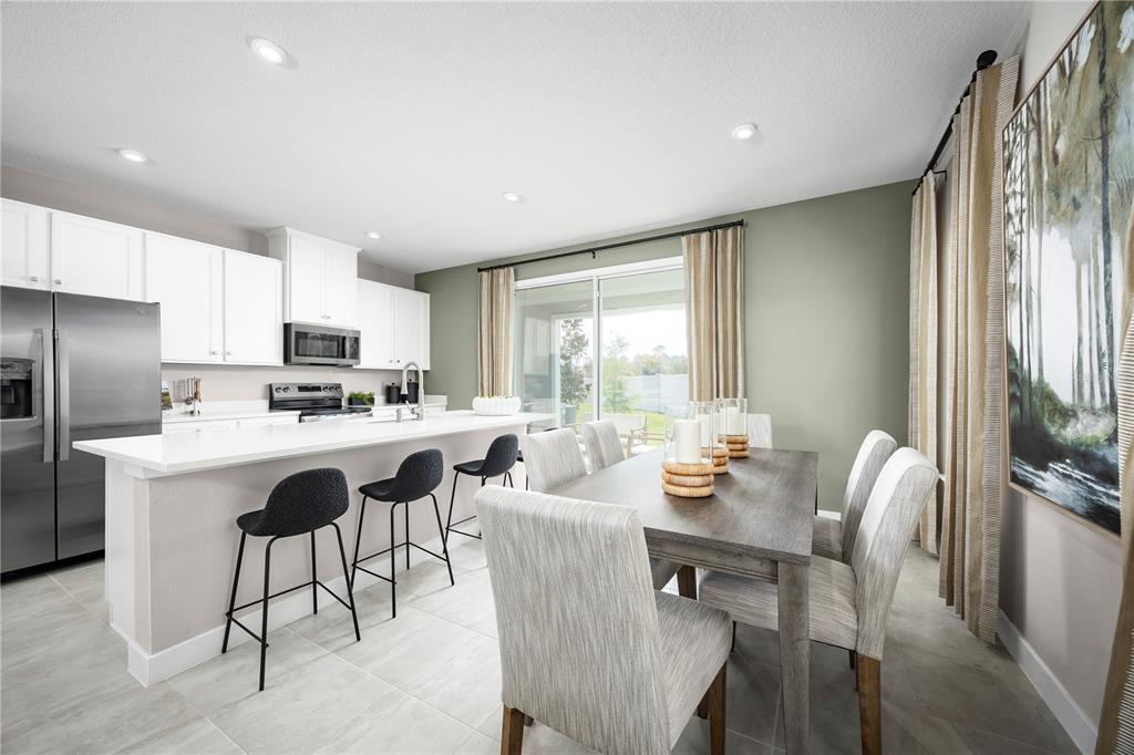 A kitchen with white cabinets and an island next to a dining area with chairs — 1652 SWEET SAPLING COURT, DAVENPORT, FL